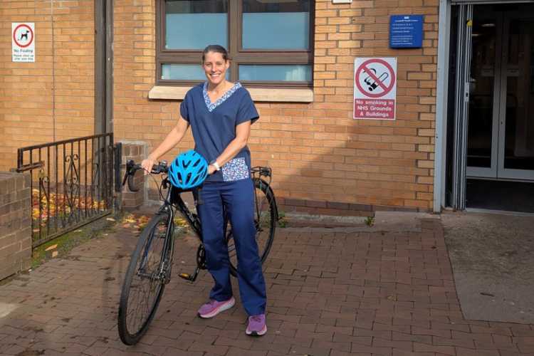 NHS health visitor, Kirsty, pictured smiling with her bike outside the health centre where she works